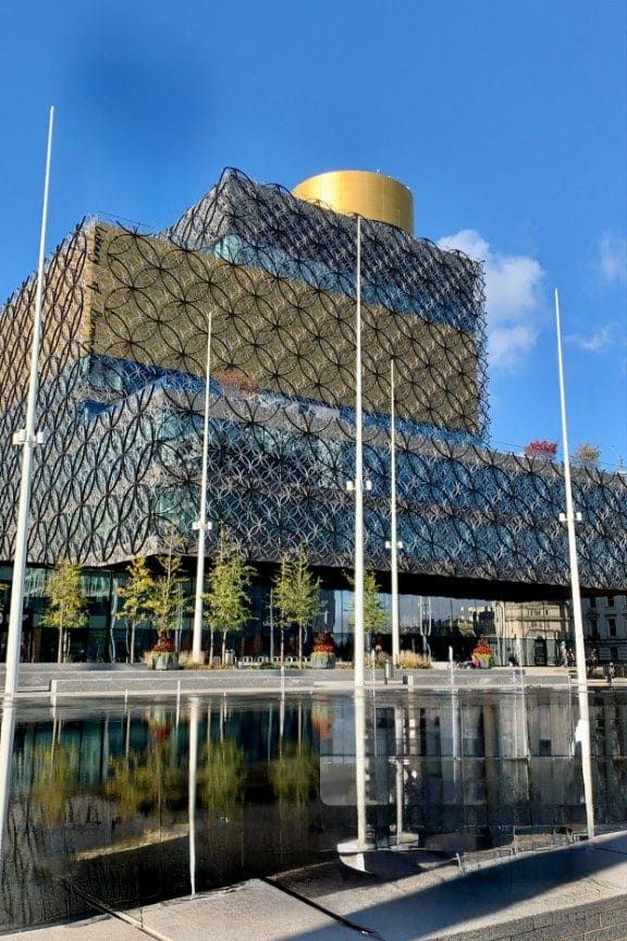 Library of Birmingham’s patterned metal facade and gold drum, reflected in the Centenary Square pool